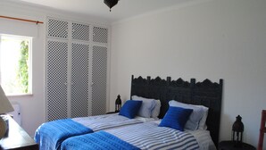 Une chambre à coucher avec un lit, une table de chevet, une lampe et une fenêtre donnant sur un paysage verdoyant.