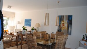 Un coin repas avec des meubles en osier, une table en verre et des lampes suspendues.