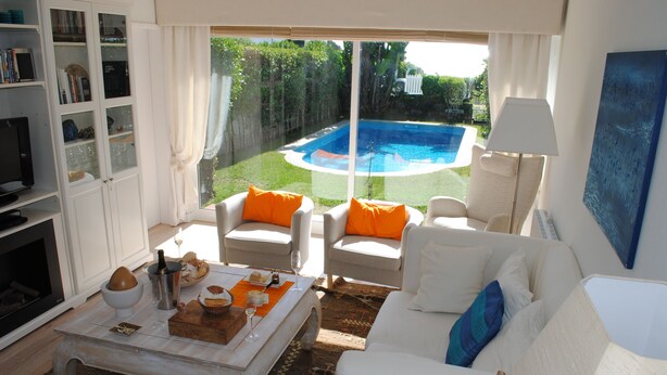 Un salon avec vue sur la piscine, des meubles blancs et une bibliothèque.