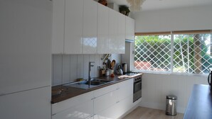 Une cuisine moderne avec des meubles blancs, un plan de travail en bois, des appareils électroménagers en acier inoxydable et une fenêtre donnant sur un paysage verdoyant.