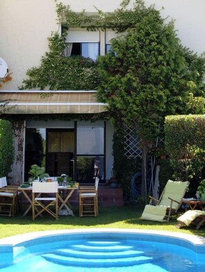 A two-story house with a covered patio, a swimming pool, and outdoor furniture.