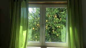 A window with green curtains, a view of a tree with yellow fruits, and a wooden window frame. - Beautiful detached villa with private pool, FibreWi-fi, garden, games room & BBQ (Souto)