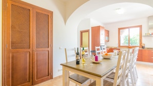 Un comedor con una mesa de madera, sillas blancas y una cocina al fondo.