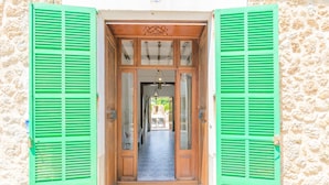 Una puerta de madera con contraventanas verdes, suelo de baldosas y pared de piedra.