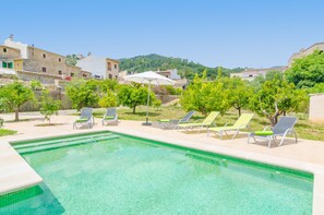 Ein Swimmingpool mit Liegestühlen und Sonnenschirmen, umgeben von Grünflächen und Gebäuden.