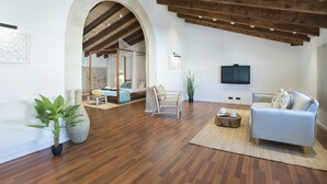 A spacious living area with wooden flooring, a white sofa, a wooden coffee table, and a large potted plant.