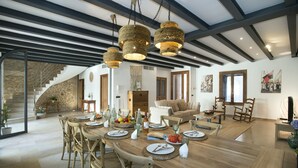 A spacious dining area with a long wooden table, multiple chairs, and hanging light fixtures.