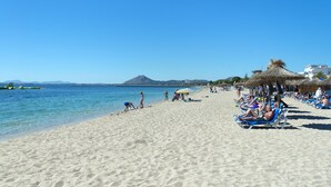 A beach with clear blue water, people sunbathing, and a mountain in the background.