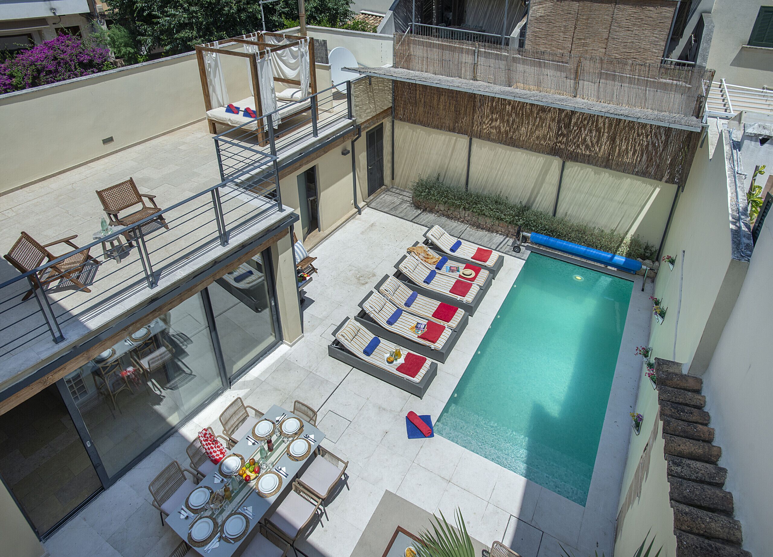 A rooftop pool area with lounge chairs, a dining table, and a covered seating area.