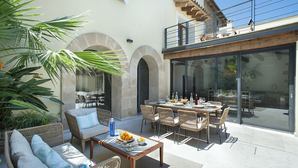 An outdoor patio with wicker furniture, a dining table, and a large glass door leading to a balcony.