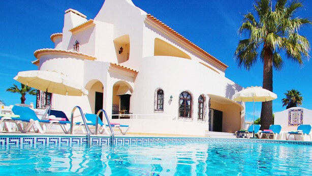 A white building with a pool, blue lounge chairs, and palm trees. - Family retreat with heatable pool and BBQ (Albufeira)