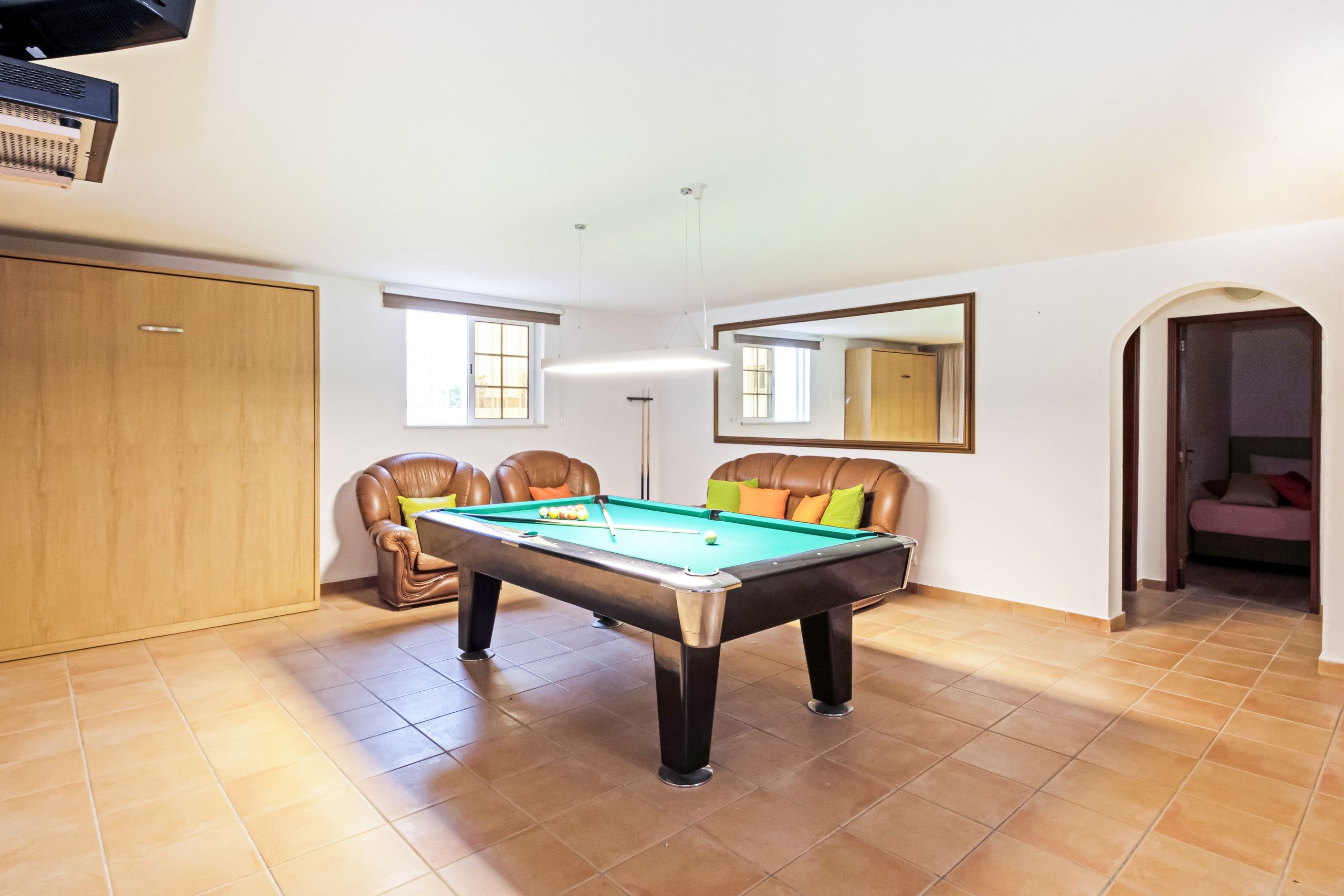 A pool table in a room with a wooden wardrobe, a mirror, and a door leading to another room.