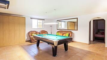 A pool table in a room with a wooden wardrobe, a mirror, and a door leading to another room.