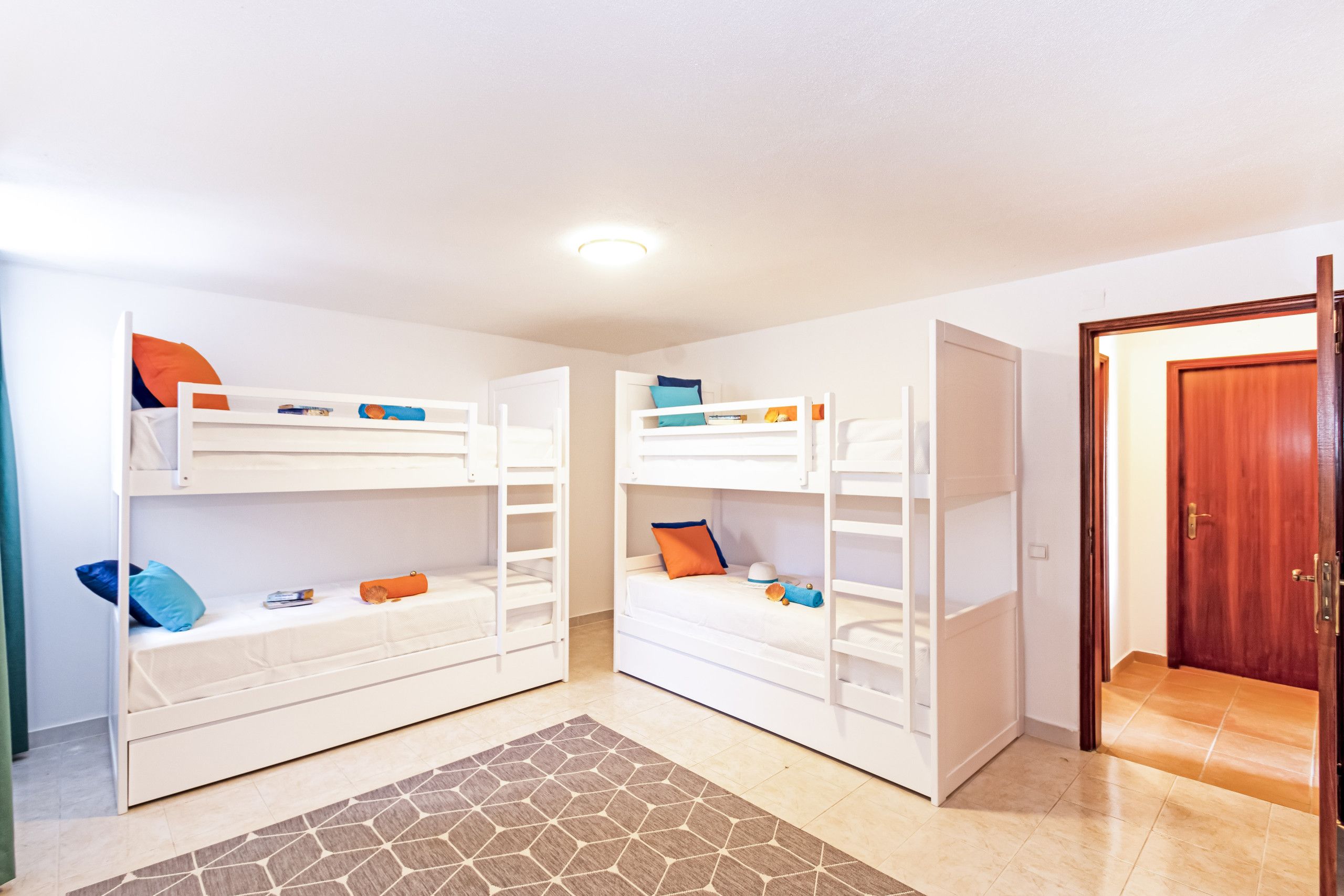 A room with two bunk beds, a wooden door, and a patterned rug.