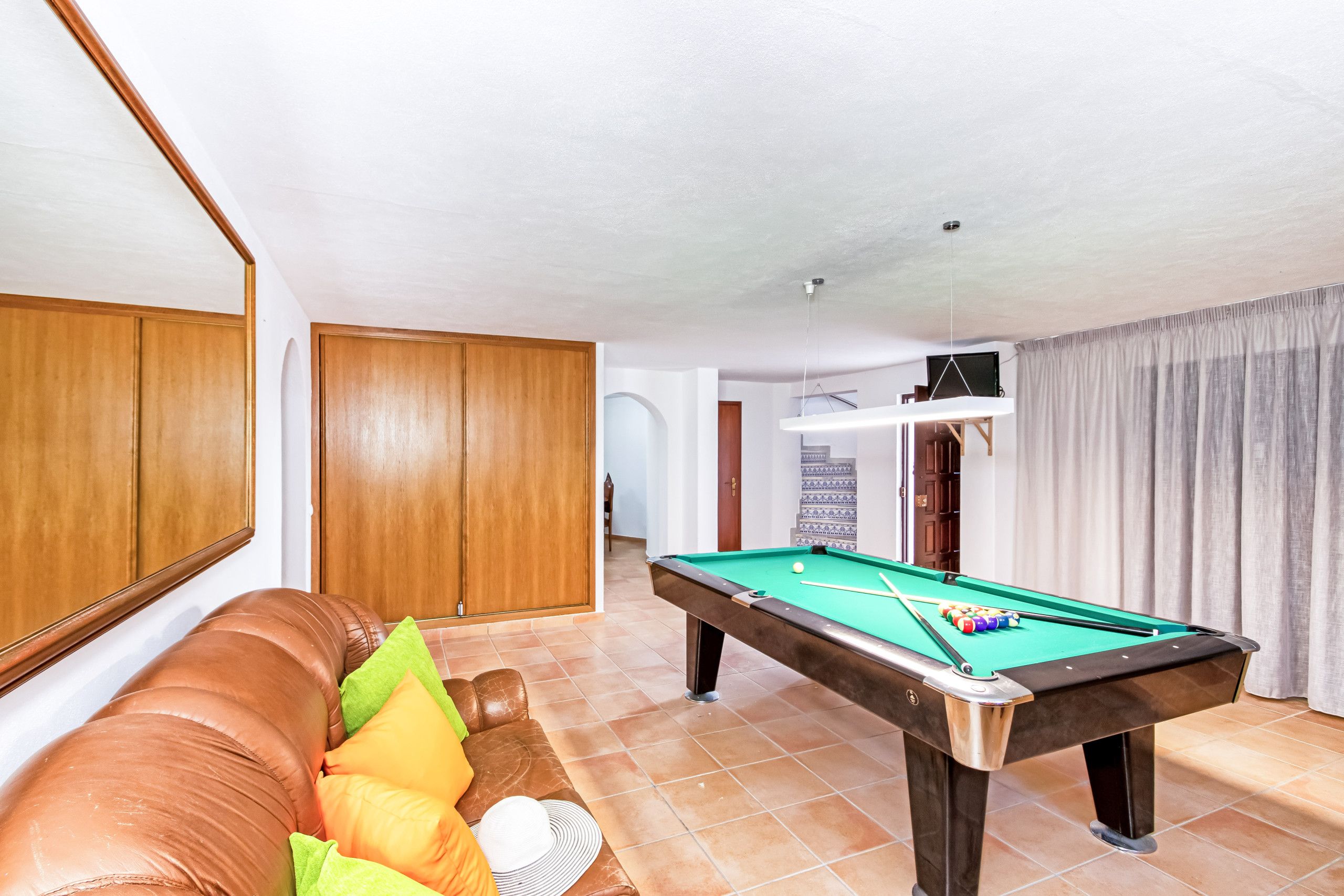 A pool table in a room with a brown leather sofa and a wooden door.