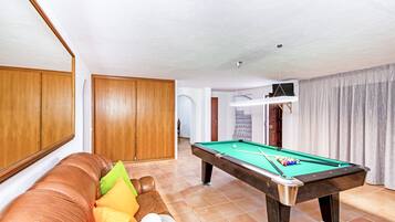 A pool table in a room with a brown leather sofa and a wooden door.