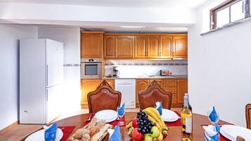 A dining area with a table set for two, a kitchen in the background, and a refrigerator to the left.