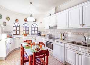 Une cuisine avec des meubles blancs, une table à manger avec des chaises, une machine à café et un évier.
