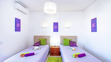A twin room with two beds, a nightstand, a green rug, and wall-mounted light fixtures.