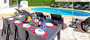 An outdoor dining area with a pool in the background.