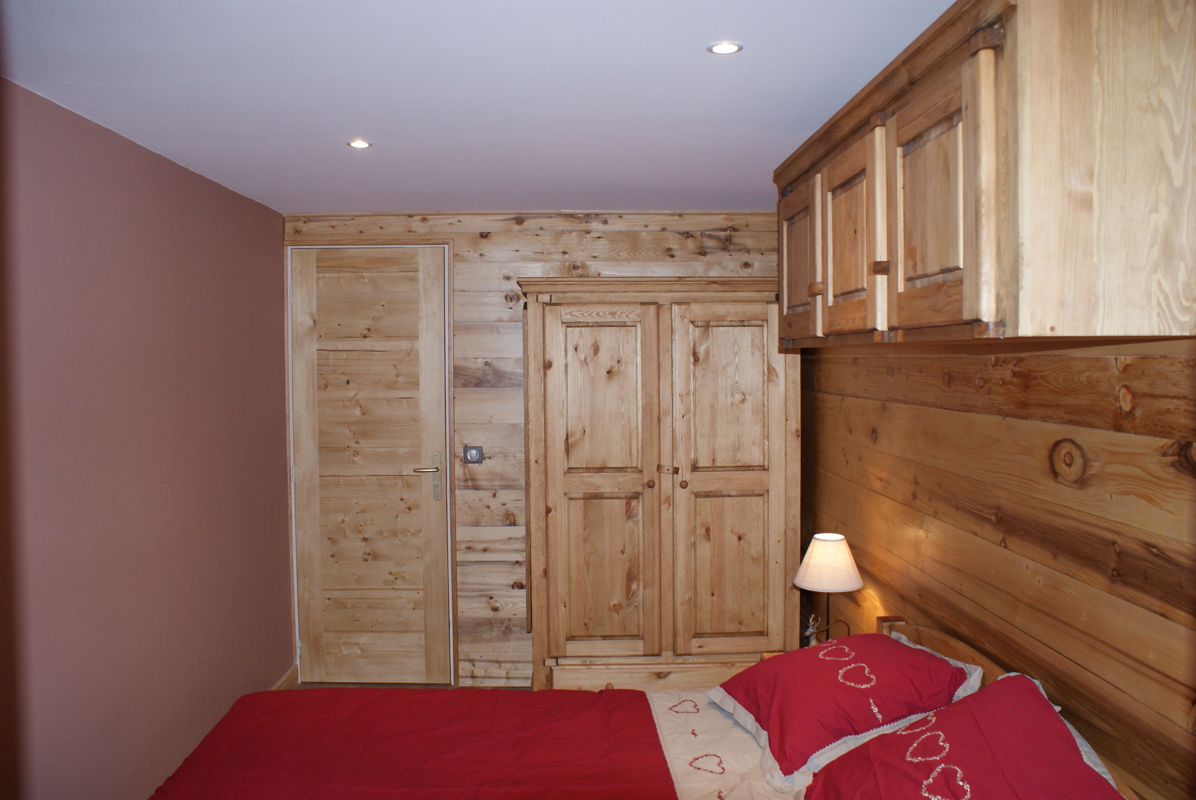 A bedroom with wooden panel walls, a bed with red bedding, and a nightstand with a lamp.