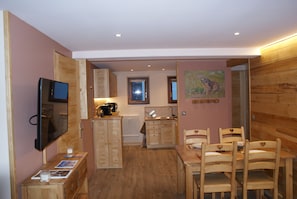 A compact room with wooden furniture, a television, a small kitchen area, and a painting on the wall.