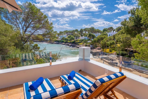 Un balcon avec deux fauteuils de jardin, une balustrade en verre et une vue sur la mer et les bâtiments.