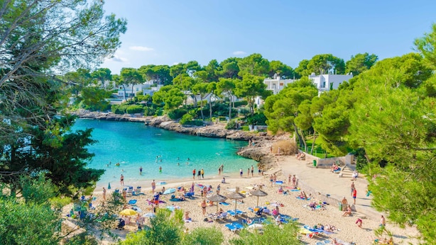 Ein Strand mit klarem türkisblauem Wasser, umgeben von üppiger Vegetation und weißen Gebäuden.