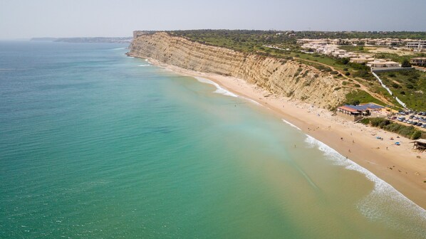 Une plage côtière avec une falaise, une étendue de sable et une rangée de bâtiments.
