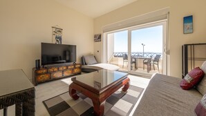 Een woonkamer met een televisie, bank en een balkon met tuinmeubilair.