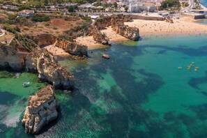 Vue aérienne d’une zone côtière avec de hautes falaises rocheuses, des eaux turquoise limpides et une plage de sable.