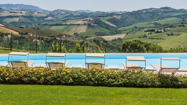 Zona de piscina con sillones de descanso y vistas a colinas onduladas y viñedos.