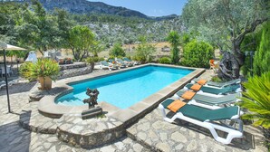 Une piscine entourée de chaises longues, de verdure et dominée par un paysage montagneux.