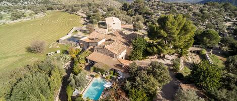 A villa with a swimming pool surrounded by greenery, set in a hilly landscape with mountains in the background.