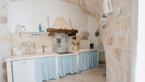 A compact kitchen with a white countertop, blue curtains, and stone walls.