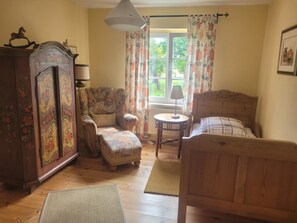Relax in a cozy space with a traditional bed, nightstand, and small table, complemented by a floral-patterned armchair and ottoman.