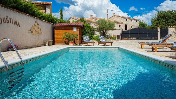 Una piscina con sillas de descanso, una cabaña de madera y un muro de piedra con el nombre 'JUSTINA'.