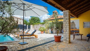 Un patio de piedra con piscina, sillas de descanso y sombrillas.
