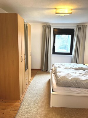 Comfortable bedroom with a large wardrobe, a bed, and a window with curtains.