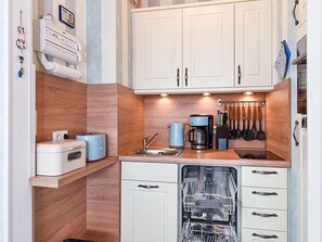 A compact kitchen with white cabinets, a dishwasher, a coffee maker, and a knife block. - Apartment "Little Pearl" - Melanie Berres Apartment "Little Pearl" (Esens)