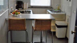 Kompakti keittiö, jossa on ruokailutila, kahvinkeitin ja ikkuna, jossa on sälekaihtimet.