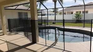 Una piscina amb una tanca de protecció metàl·lica, envoltada d'un porxo cobert que ofereix vistes a cases properes i un jardí.