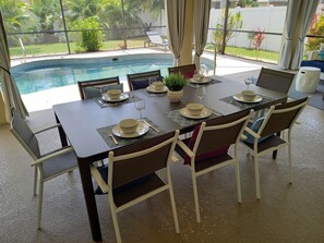 Comedor con vistas a una piscina, una mesa dispuesta para cuatro personas y una planta en maceta.