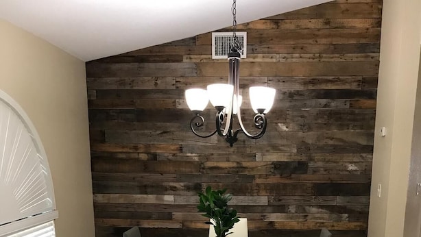Una zona de menjador moderna amb una taula blanca, cadires negres i una paret decorativa de fusta.