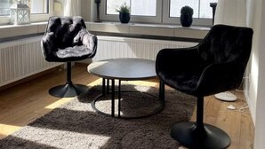 Uma sala de estar moderna com uma janela grande, uma mesa de centro redonda e duas cadeiras pretas.