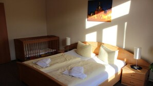 A hotel room with a large bed, a wooden crib, a nightstand with a lamp, and a painting on the wall. - Apartment 3 - 3 Bedrooms - 110 m² - Wifi - Dog allowed (Wernigerode)
