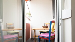 A balcony with a wooden table and chairs, a wicker basket, and a view of the outside.