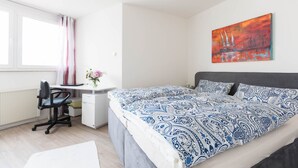 A bedroom with a bed, a desk, a chair, a radiator, and a window with curtains.