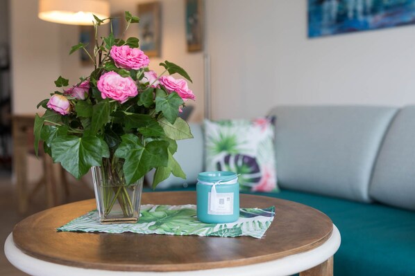 Un vase avec des fleurs roses sur une table ronde, une bougie turquoise et un set de table vert à motifs de feuilles.