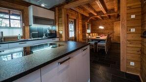 A modern kitchen with granite countertops, white cabinetry, and a dining area with wooden tables and chairs. - Comfortable wooden house in the heart of Saxon Switzerland above Rathen (Bad Schandau OT Waltersdorf)